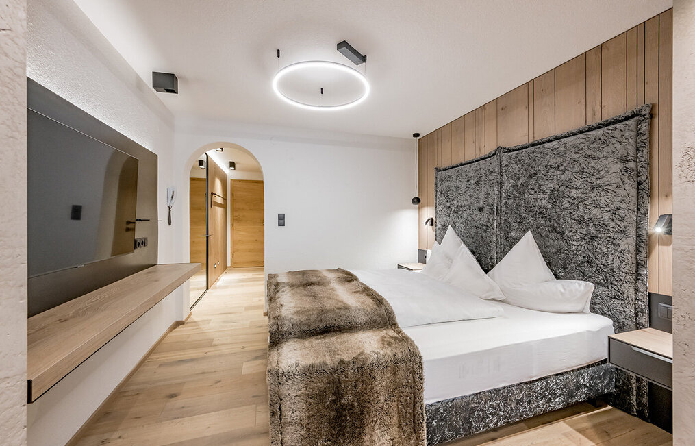 Modern hotel room with wooden flooring, a made bed, a wall-mounted TV and minimalist lighting. Light wood tones and soft textures create a cozy atmosphere.