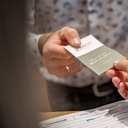 One person is handing a card to another person across a counter. A form labeled "Guest Sheet" is lying on the counter.