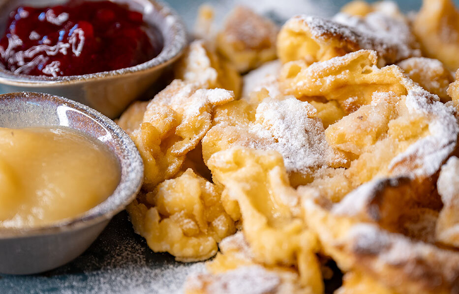 A plate of Kaiserschmarrn scrambled pancake, dusted with powdered sugar and served with small bowls of stewed red fruit and applesauce.