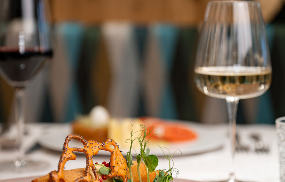 A gourmet dish arranged on a plate with grilled asparagus, potatoes and a side dish, served on a table with glasses of red and white wine in a stylish restaurant setting.