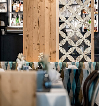 The restaurant's stylish interior features patterned partition elements and bench seating, as well as tables set with white linens, glassware and flowers. In the background, the bar is stocked with bottles and glasses.