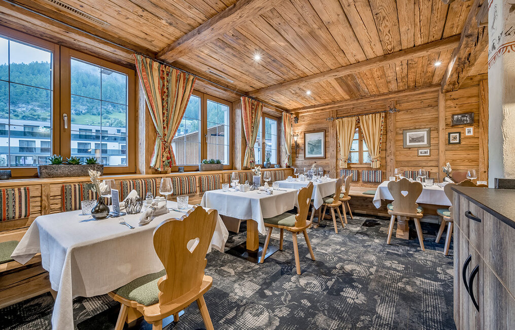 Cozy restaurant featuring a wooden interior, large windows, white tablecloths, set tables, upholstered bench seating and mountain views. A warm, inviting atmosphere with rustic décor elements.