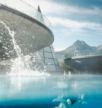 A swimmer glides underwater in a clear blue pool with modern, curved buildings and mountains in the background. Beneath a partly cloudy sky, a fountain of water rises above the pool's surface.