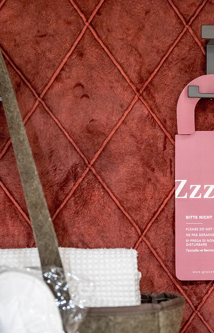 An Haken vor einer rot gesteppten Wand hängen ein rosa Türhänger und eine Tasche mit Handtüchern.