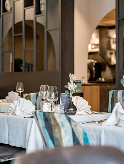 Elegant dining room featuring neatly set tables, striped upholstered chairs, folded white napkins, wine glasses and decorative vases. A warm, inviting atmosphere in the background, complemented by modern design elements.