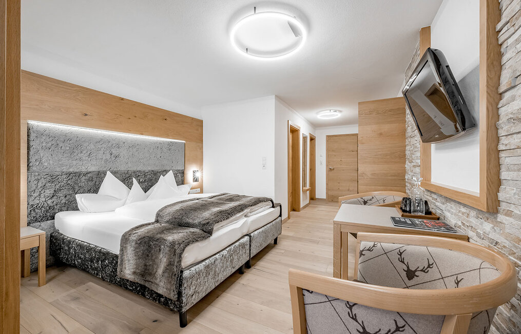Modernes Hotelzimmer mit einem Doppelbett, einer Felldecke, Holzböden, einem kleinen Tisch mit Stühlen, einem an der Wand montierten Fernseher und einer neutralen Einrichtung. Das Zimmer wirkt hell und gemütlich.