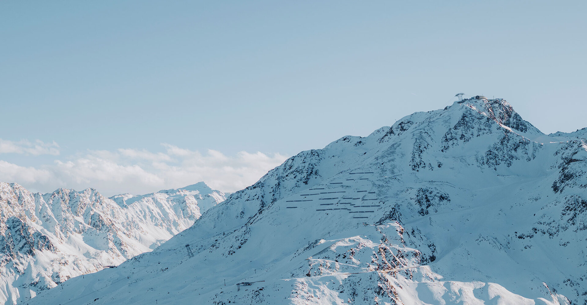 Snow-covered mountain peaks under a bright blue sky with sunlight highlighting the rugged slopes and  mountain gondola lift on the nearest mountain.