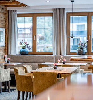 A cozy seating area with brown chairs, a wooden table with a small vase and a wall picture showing a cow against a mountain backdrop.