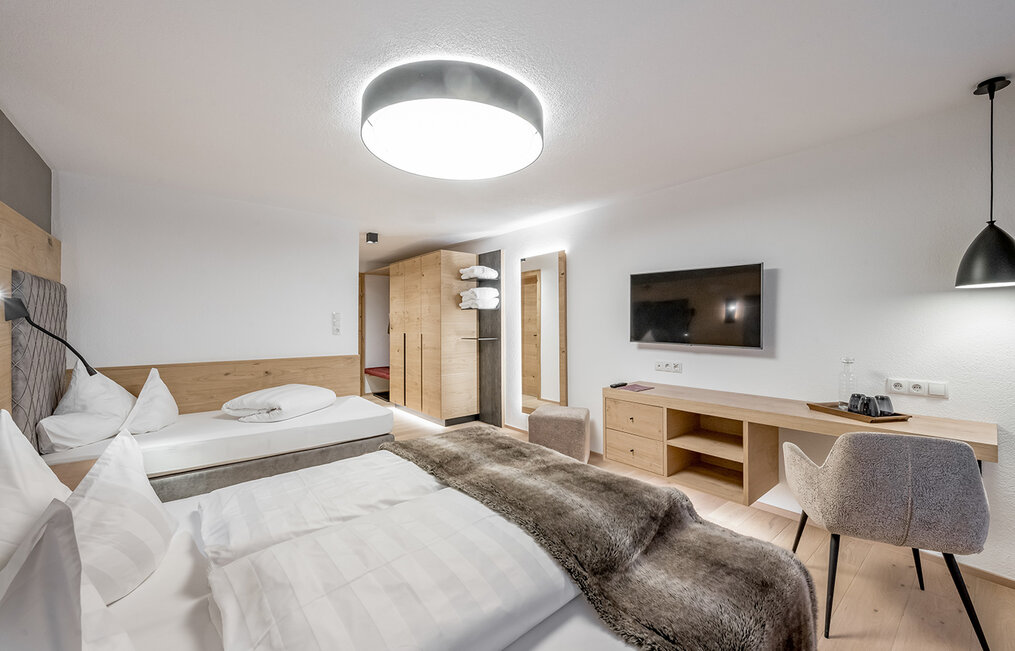 Modern hotel room with two beds, a desk, a chair, a wall-mounted TV, a large ceiling light, wooden furniture and neutral décor.