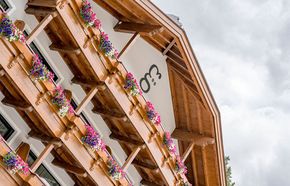 The hotel building features balconies lined with flower boxes filled with colorful blooms. The hotel's branding is written on the building's white wall.