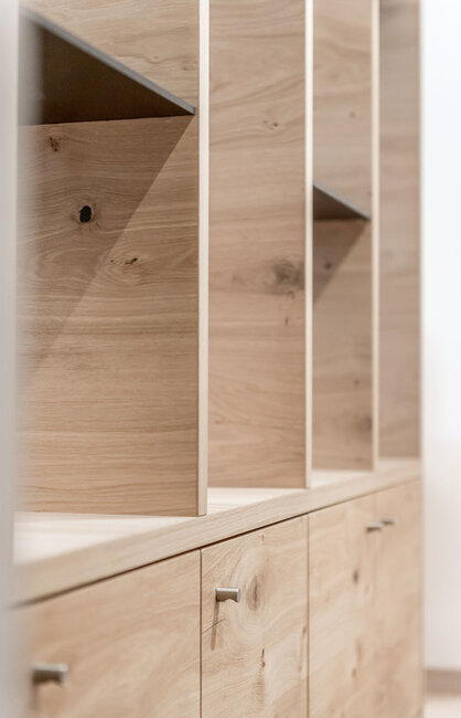 Ein helles Holzregal mit vertikalen und horizontalen Trennwänden sowie Unterschränken mit Metallgriffen, das an einer weißen Wand steht. Die Regalböden sind leer und zeichnen sich durch ein minimalistisches Design aus.
