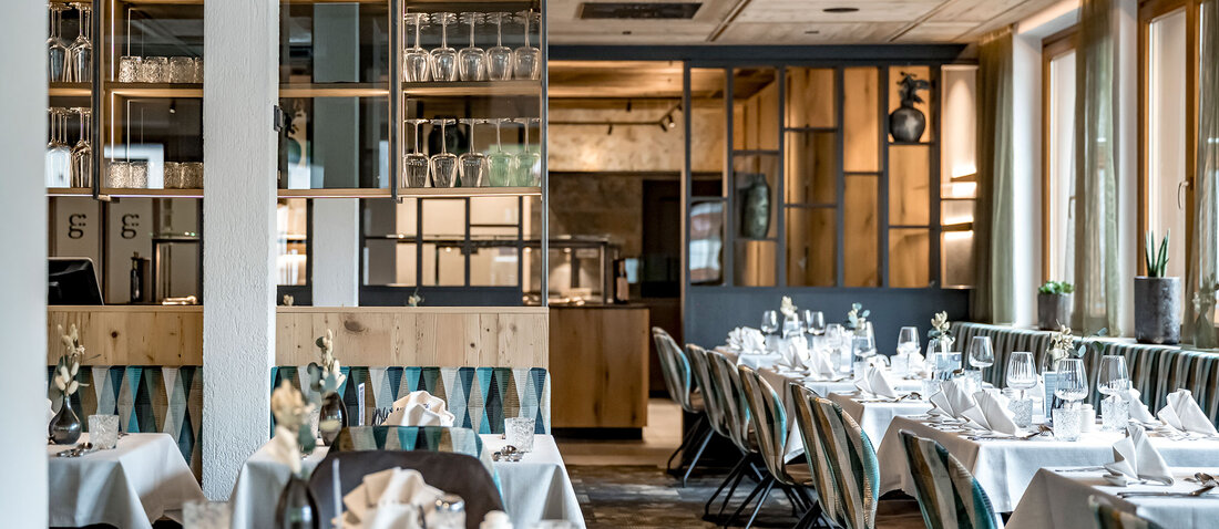 A modern restaurant interior featuring wood accents, large windows and neatly set tables with white tablecloths and folded napkins, creating an inviting and elegant dining atmosphere.