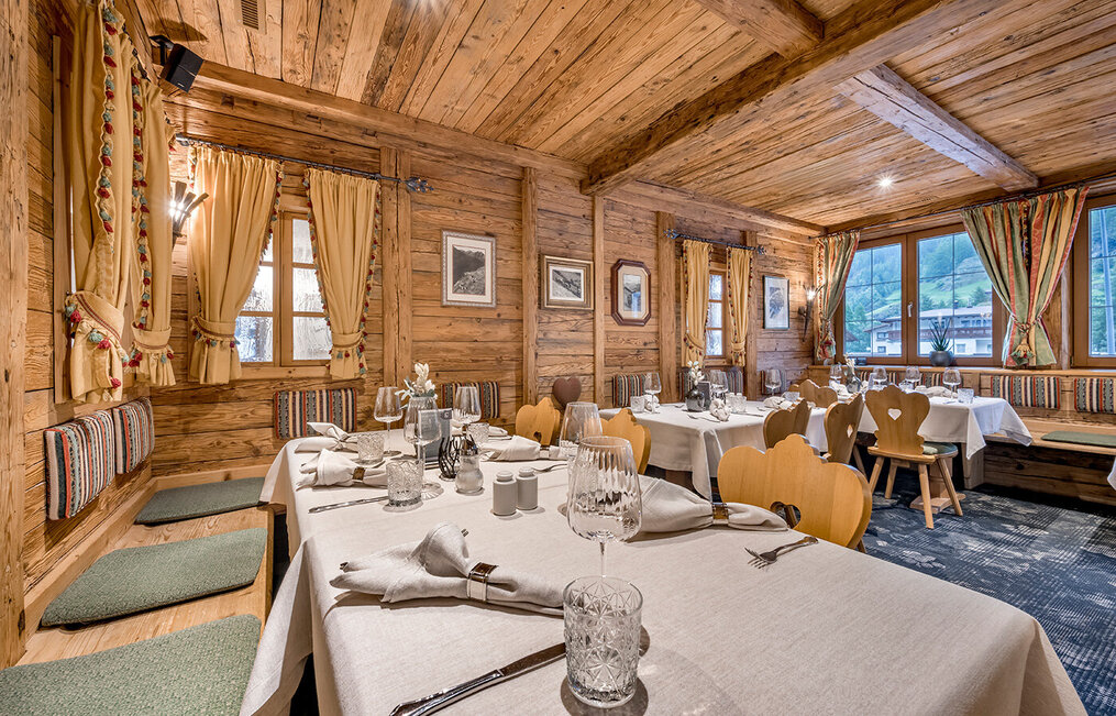 A cozy restaurant with wood-paneled walls and ceilings, where the tables are set with white tablecloths, glassware, cutlery and napkins. Daylight streams in through the windows, offering a picturesque view of the outside.