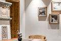 Eine gemütliche Sitzecke mit einem Holztisch, zwei braunen Stühlen, einer gepolsterten Bank, einer kleinen Vase mit Blumen, gerahmten Fotos an einer weißen Wand sowie Holzakzenten an der Decke und am Türrahmen.