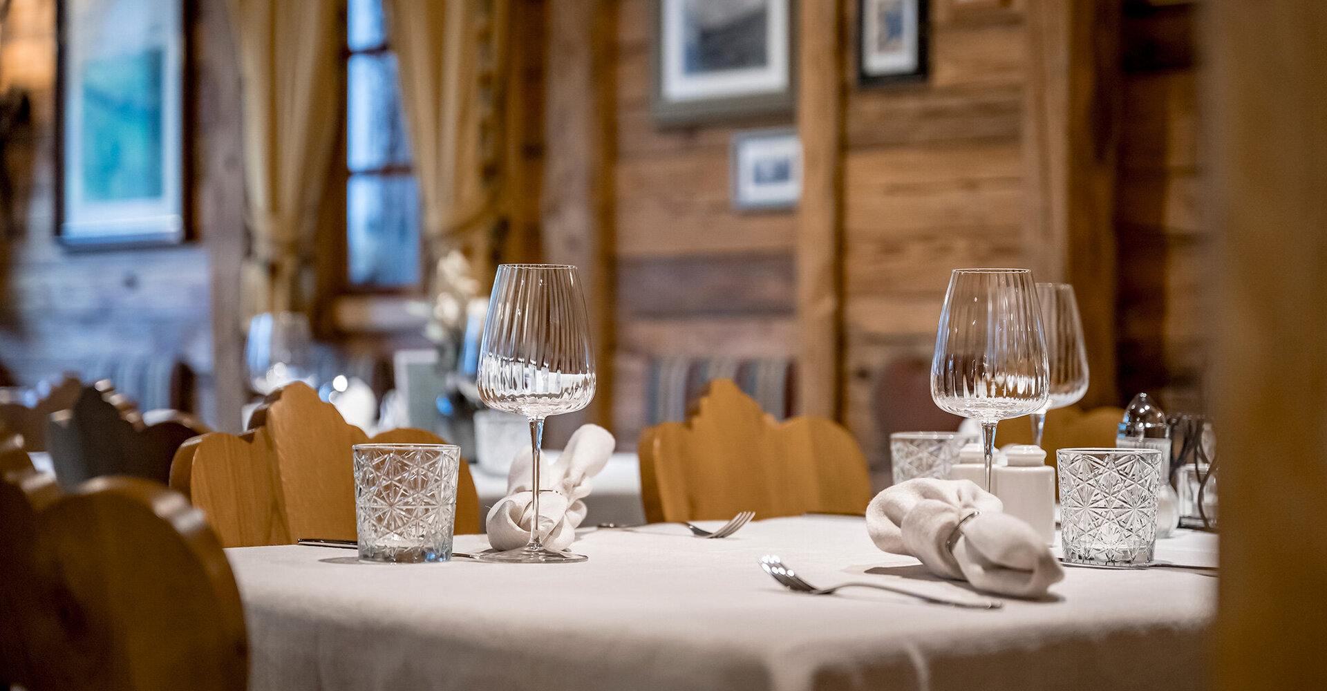 A cozy restaurant table, set with glasses, napkins and cutlery, surrounded by wooden chairs and rustic decor.
