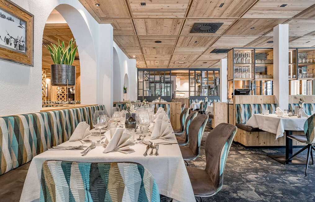 Elegant restaurant interior with a wooden ceiling, patterned upholstered chairs, white tablecloths and neatly arranged glassware and napkins on the tables. Modern décor and plenty of natural light.