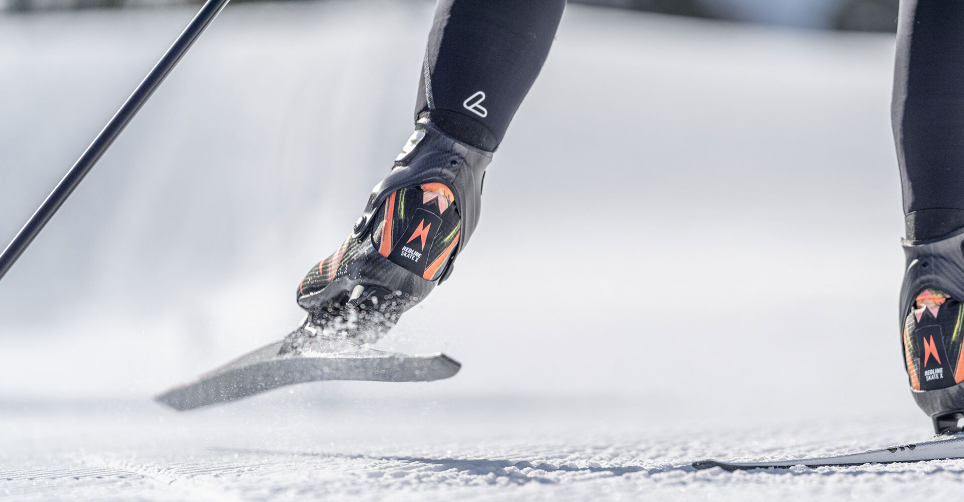Close-up of a cross-country skier's leg and skis gliding over the snow with snow being kicked up when a ski is lifted.