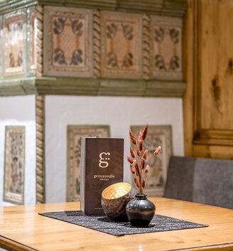 A wooden table with a black tablecloth, a vase with dried red flowers, a decorative bowl and a menu. Ornate tiles and wood panelling are in the background.