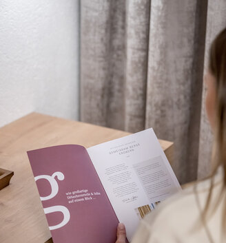 A person is sitting at a wooden table, holding an open brochure while reading it.