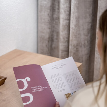 A person is sitting at a wooden table, holding an open brochure while reading it.