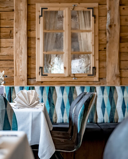 Cozy restaurant interior featuring wood-paneled walls, framed photos and tables set with white tablecloths and neatly folded napkins. Blue-and-white patterned bench seating lines the wall.