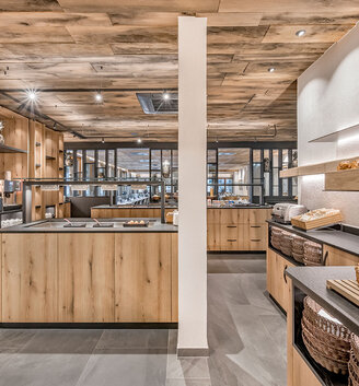 Modern buffet interior featuring wooden shelves and counters displaying various types of bread and baked goods. Light wood tones, grey flooring and a cozy atmosphere created by baskets and loaves of bread arranged on the counters and shelves.