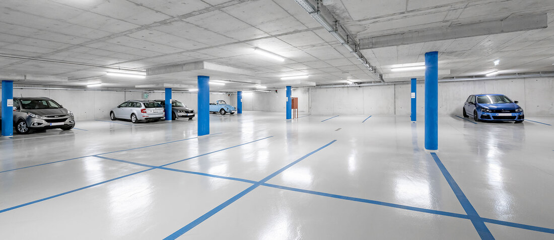 A clean, brightly lit underground garage with blue-striped parking spaces. Only a few cars are parked there, the area is largely empty and is defined by concrete pillars and a concrete ceiling.