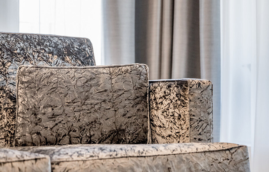 Close-up of a textured, patterned armchair in front of sheer white curtains and dark drapes, creating a modern and cozy ambiance.