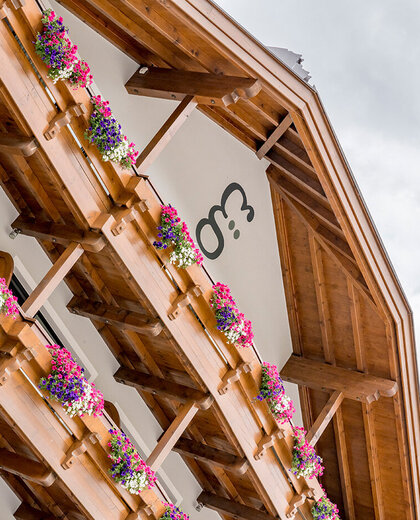 The hotel building features balconies lined with flower boxes and colorful blossoms. The hotel's branding is written on the building's white wall.