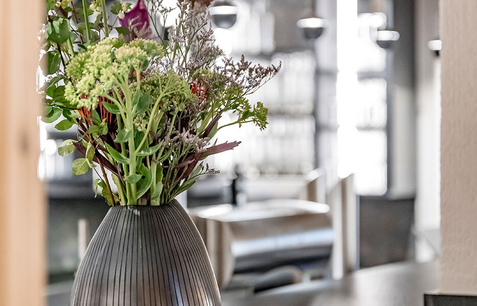 A dark, ribbed vase containing various wildflowers sits on a gray countertop in a modern kitchen, with wooden accents and pendant lights in the background.