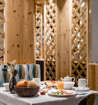 A dining table set for breakfast with pastries, juice, tea, cups and plates of food in a cozy restaurant featuring wood décor and patterned room dividers.