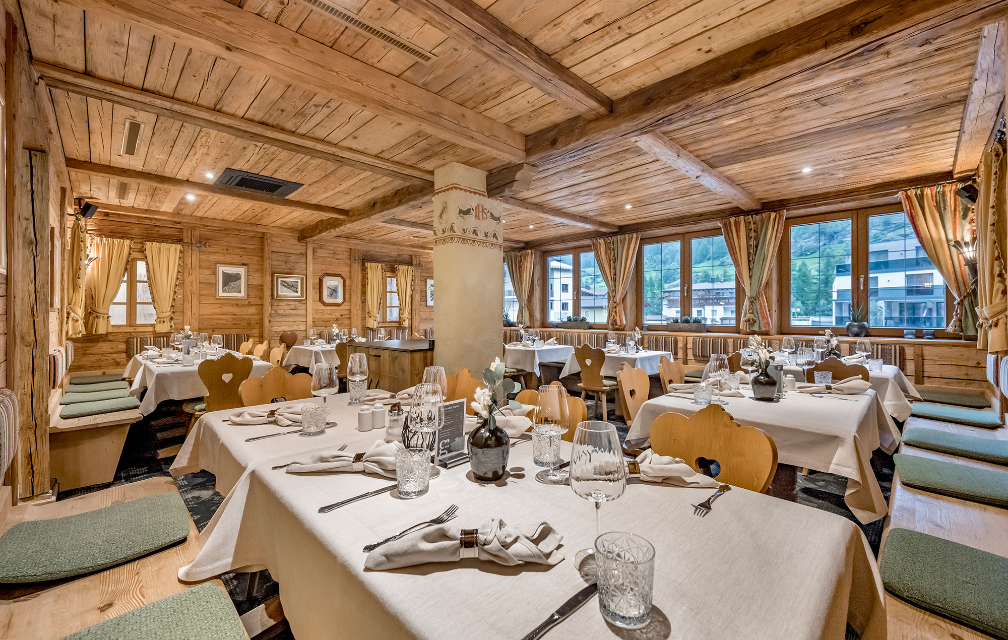 Cozy wooden restaurant interior featuring neatly set tables, wooden chairs with heart-shaped backrests and large curtained windows allowing daylight to stream in.